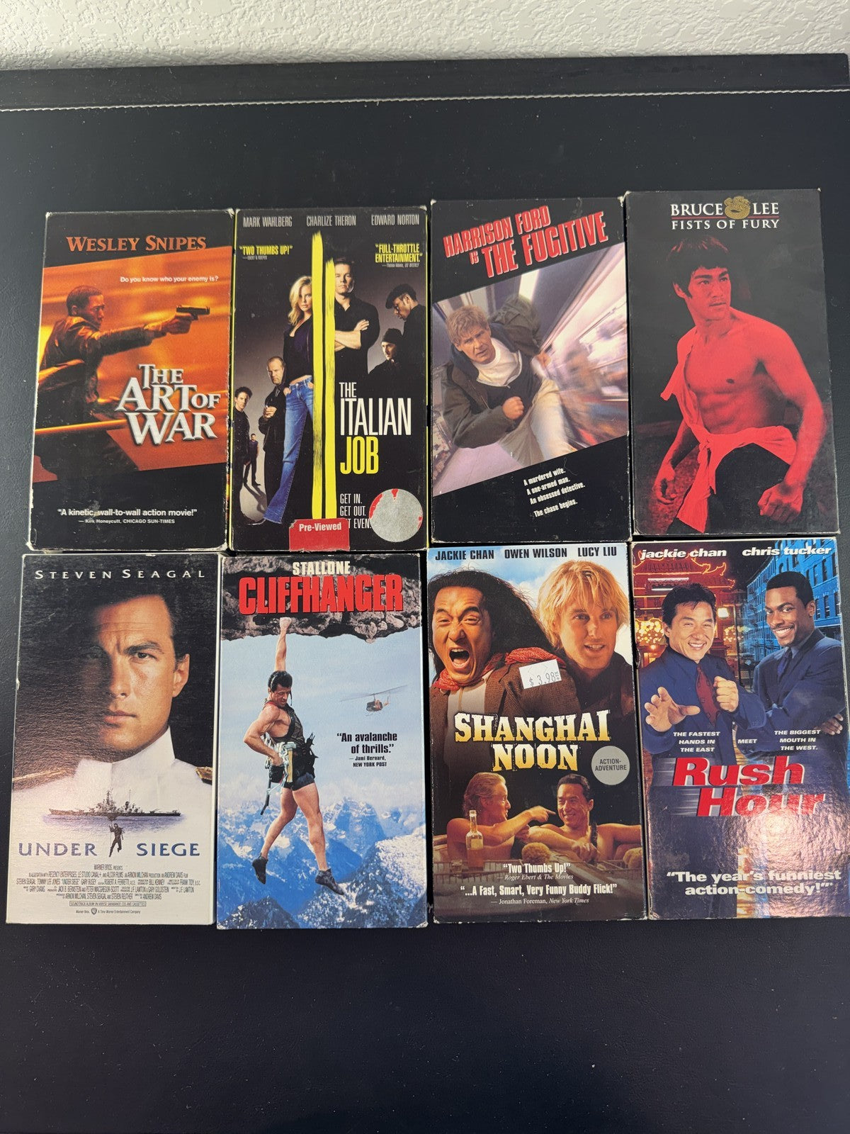 Collection of 8 vintage action movie VHS tapes including Rush Hour, Cliffhanger, and The Fugitive.