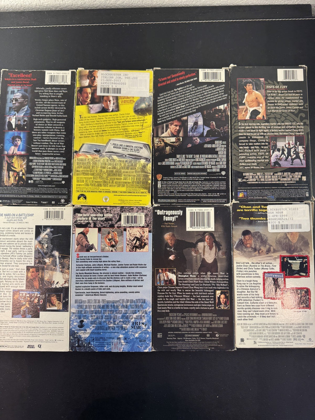 Collection of 8 vintage action movie VHS tapes including Rush Hour, Cliffhanger, and The Fugitive.