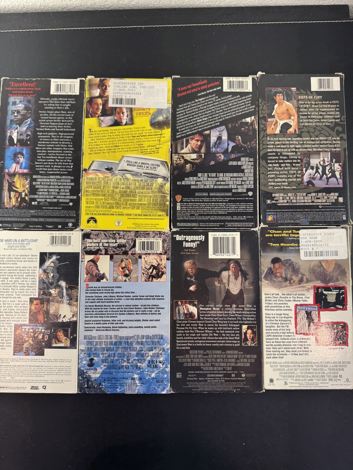 Collection of 8 vintage action movie VHS tapes including Rush Hour, Cliffhanger, and The Fugitive.
