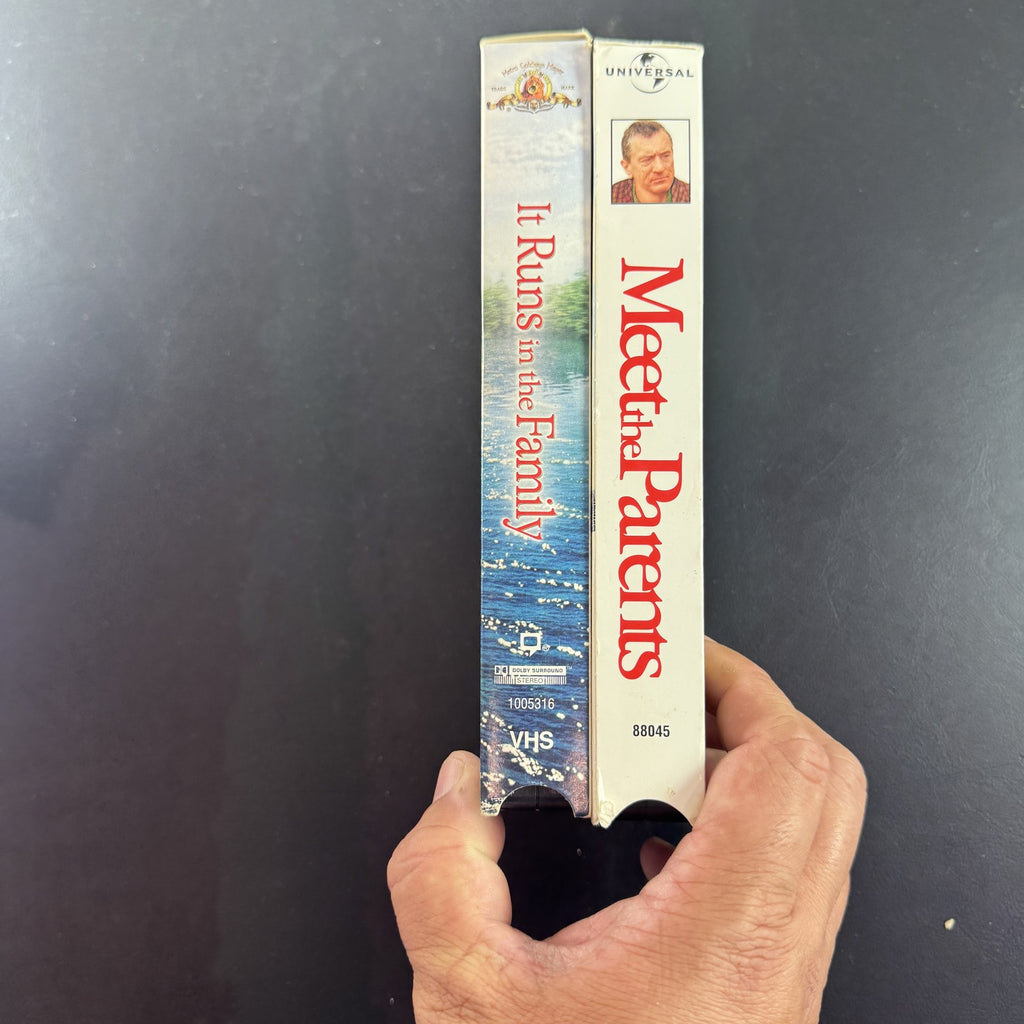 Set of two vintage comedy VHS tapes featuring Meet the Parents and It Runs in the Family in original slipcases.