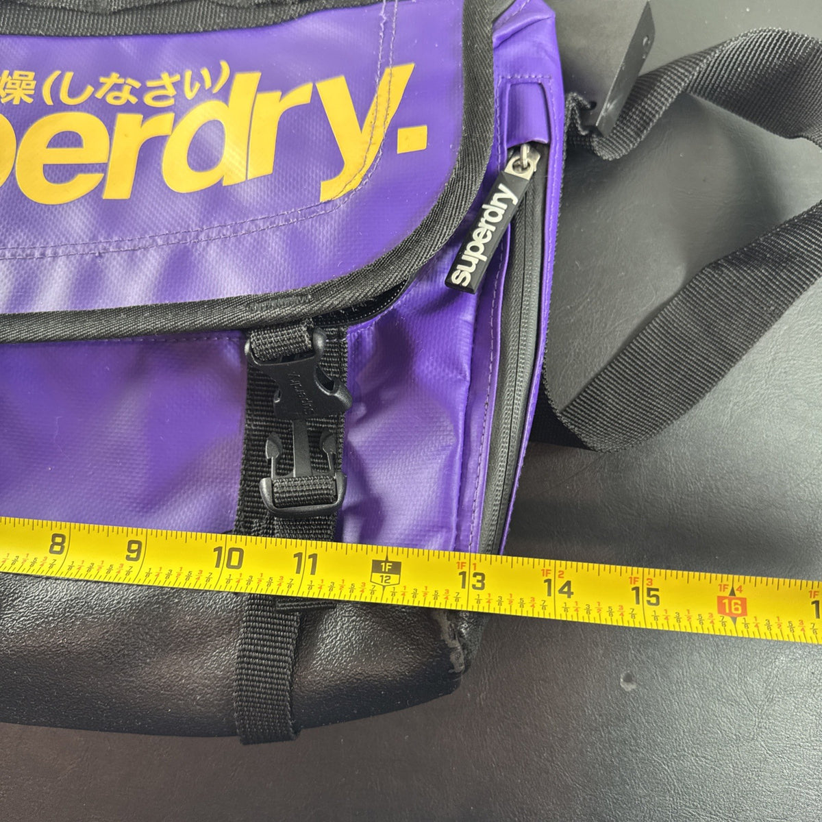 Purple and yellow Superdry tarp messenger bag with bold logo spellout and padded shoulder strap.