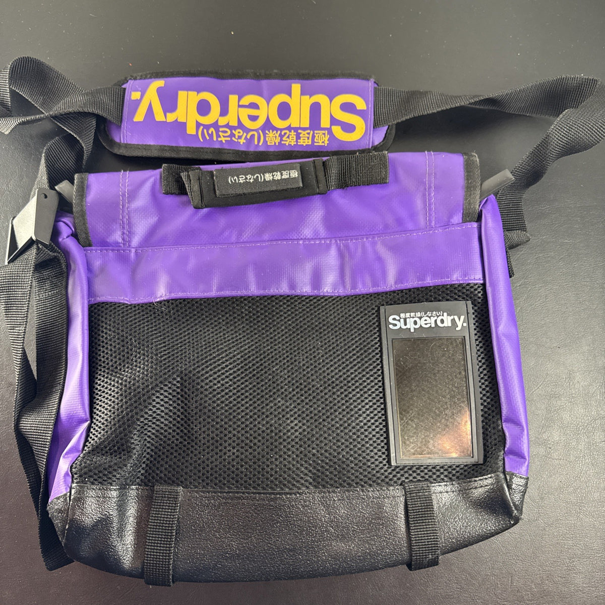 Purple and yellow Superdry tarp messenger bag with bold logo spellout and padded shoulder strap.