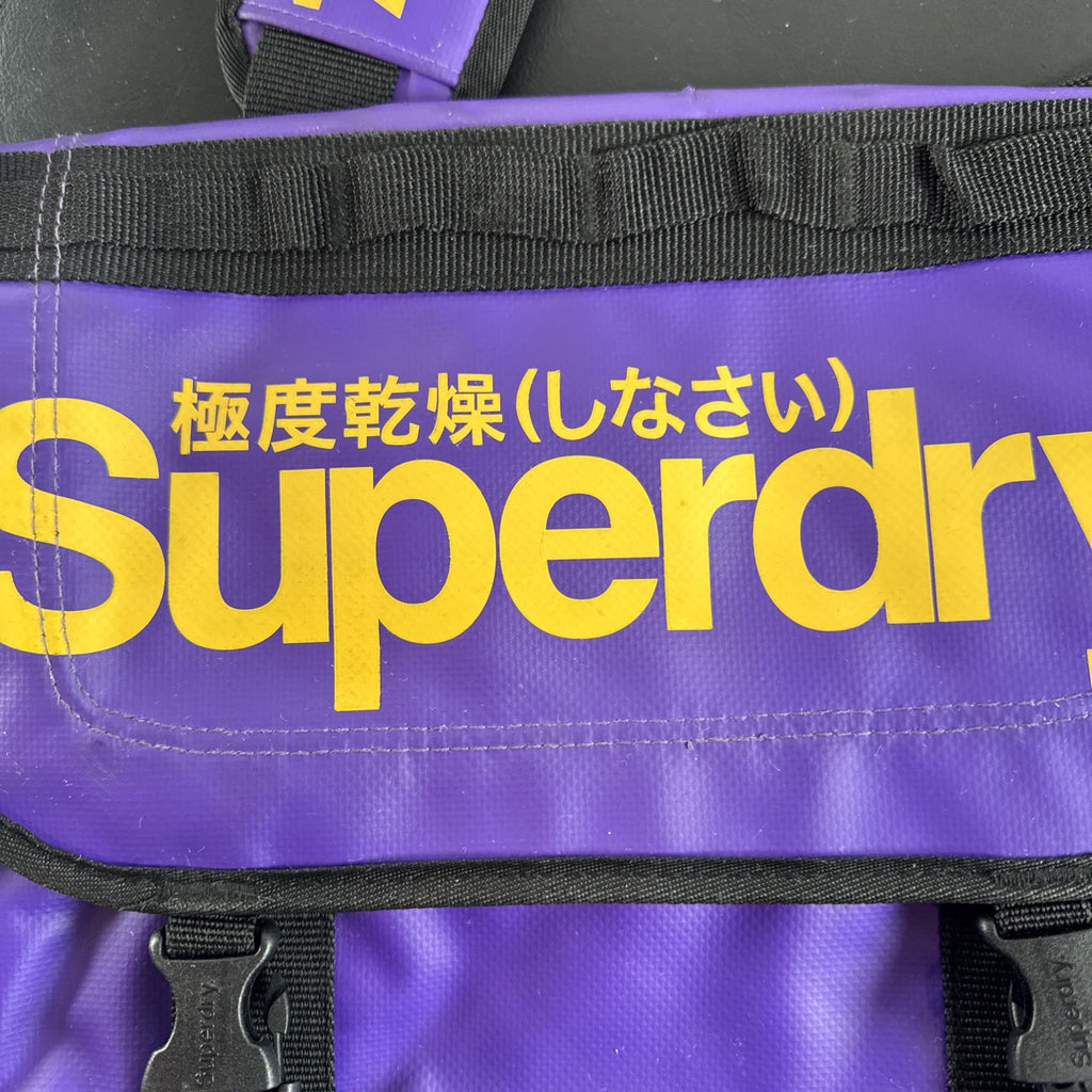 Purple and yellow Superdry tarp messenger bag with bold logo spellout and padded shoulder strap.