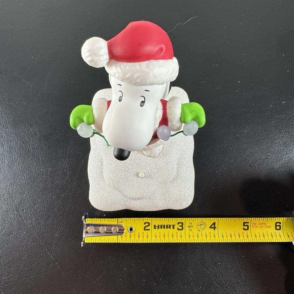 Hallmark Snoopy in Santa suit holding holiday lights on a glittery snow base tabletop figure