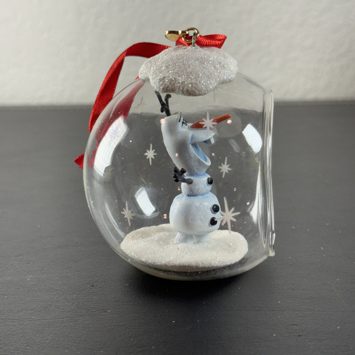 Disney Frozen Olaf glass globe diorama ornament featuring glitter snow accents and red hanging ribbon.