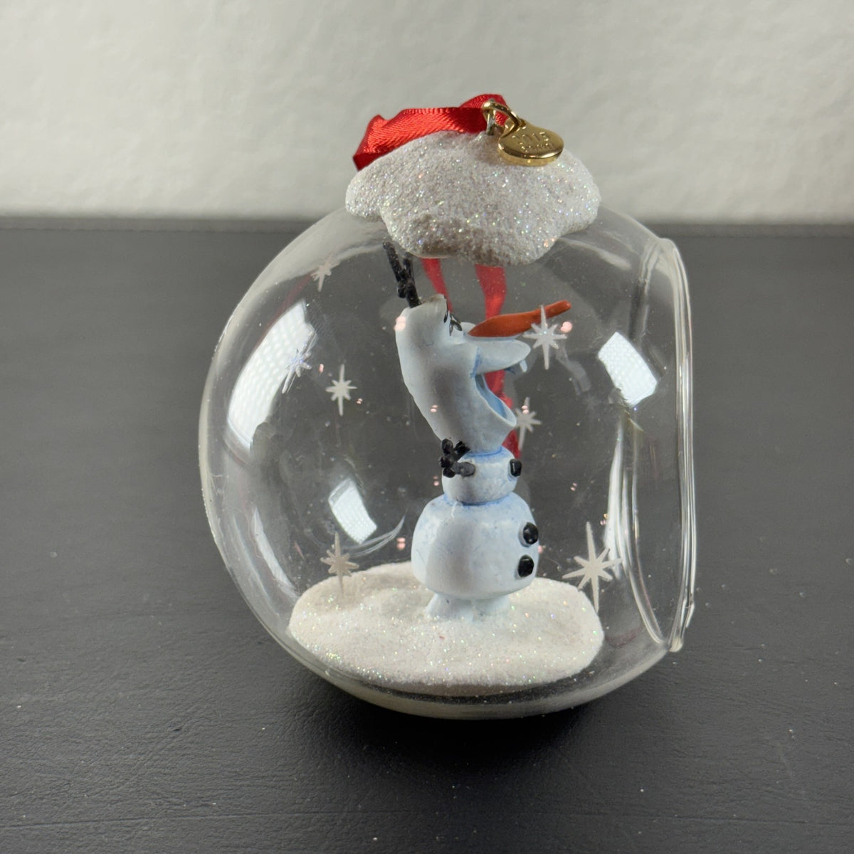 Disney Frozen Olaf glass globe diorama ornament featuring glitter snow accents and red hanging ribbon.