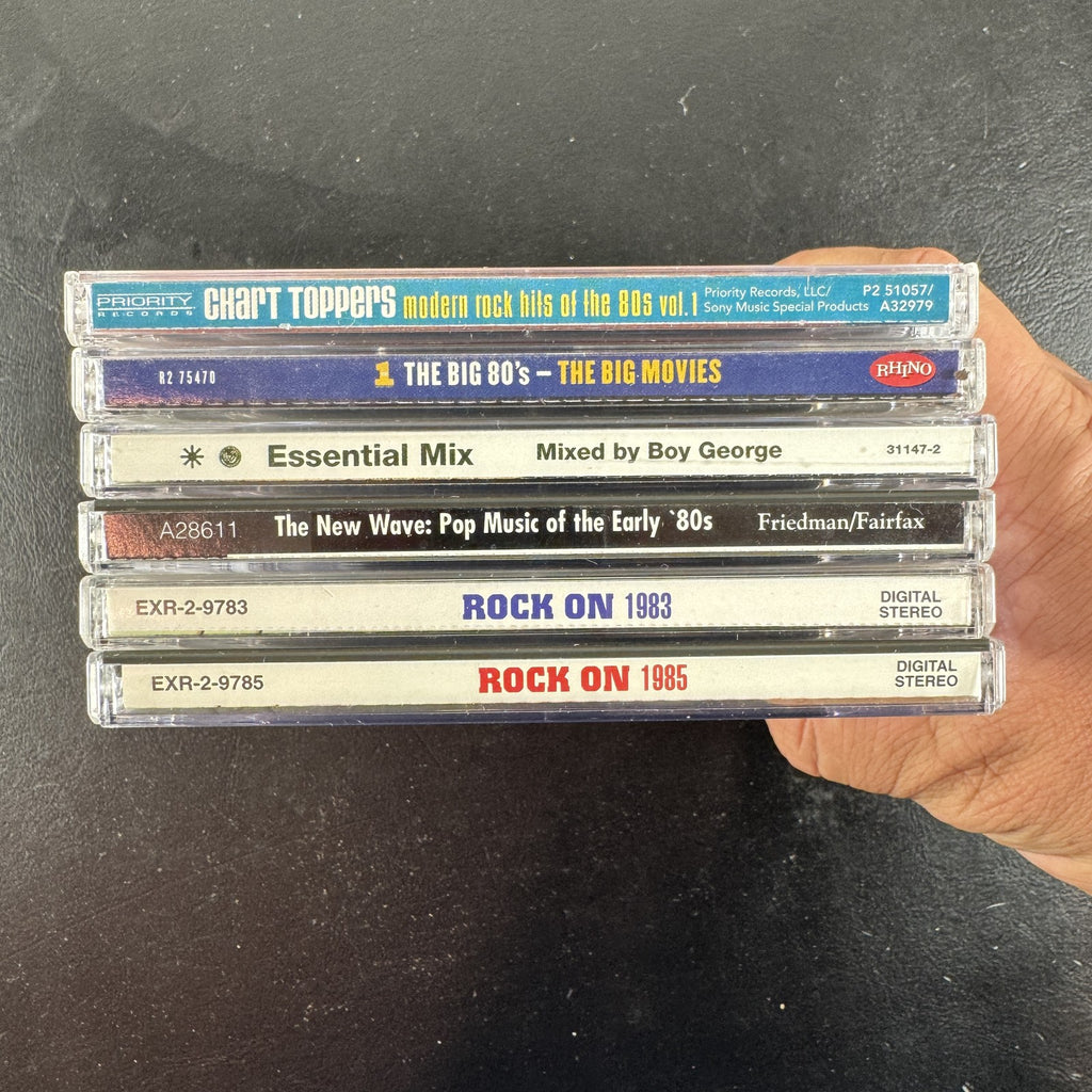 Set of 6 pre-owned 1980s compilation CDs including 80s movie hits and new wave rock collections.
