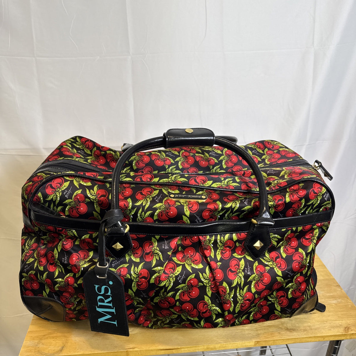 Betsey Johnson black rolling weekender duffel bag featuring a red cherry print and telescoping handle.