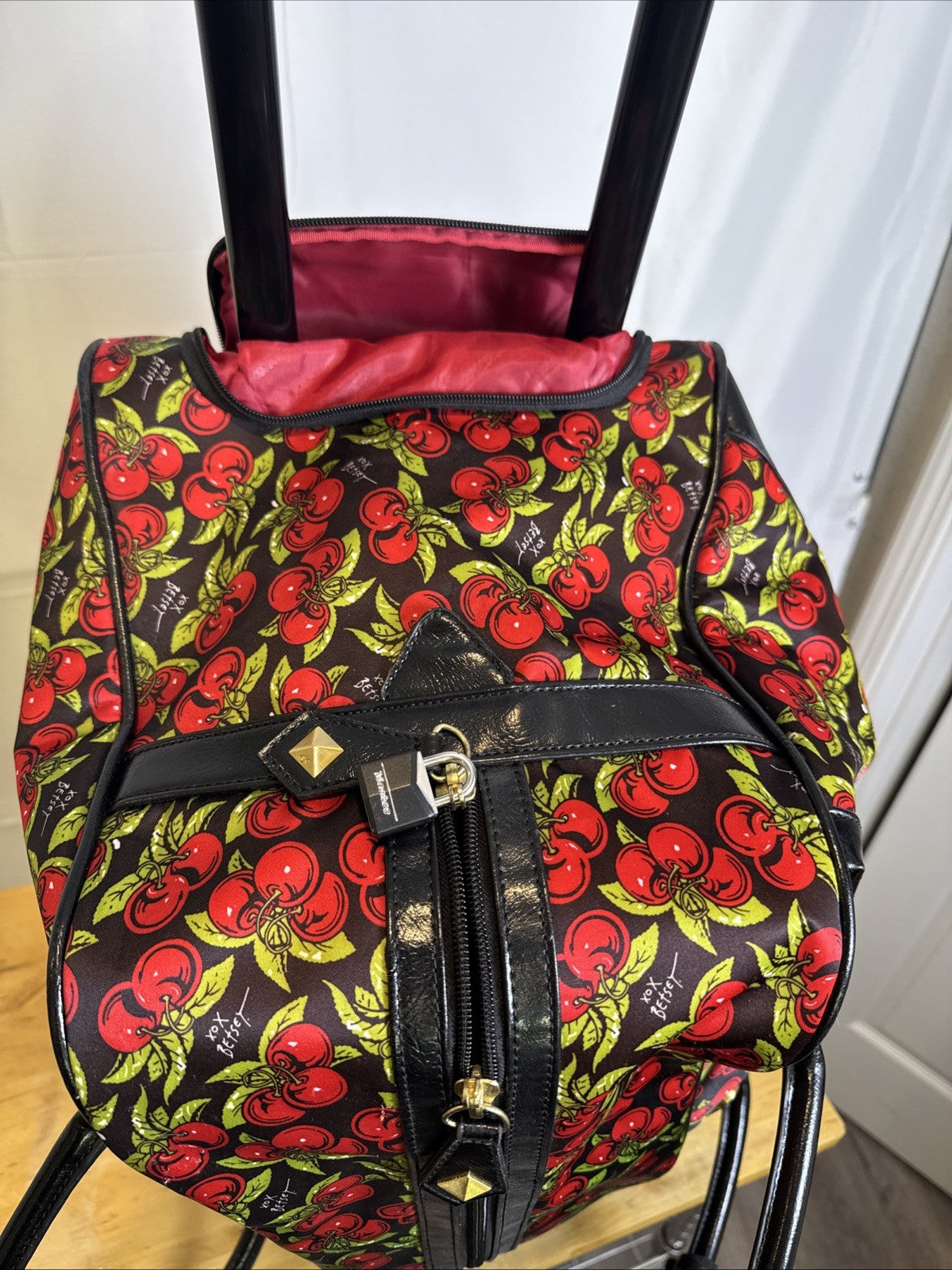 Betsey Johnson black rolling weekender duffel bag featuring a red cherry print and telescoping handle.