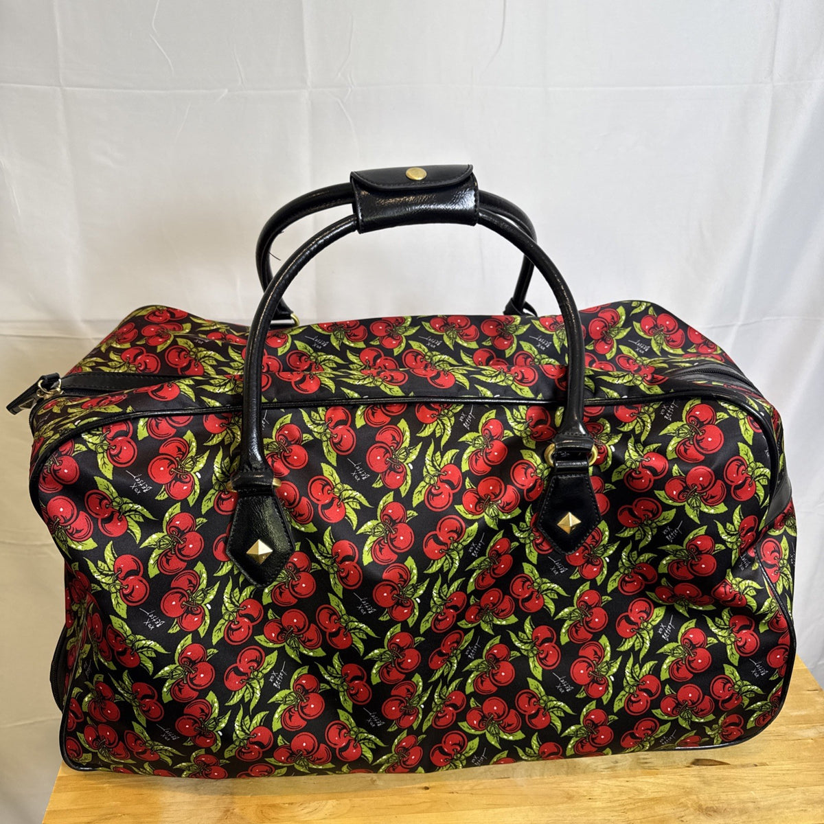 Betsey Johnson black rolling weekender duffel bag featuring a red cherry print and telescoping handle.