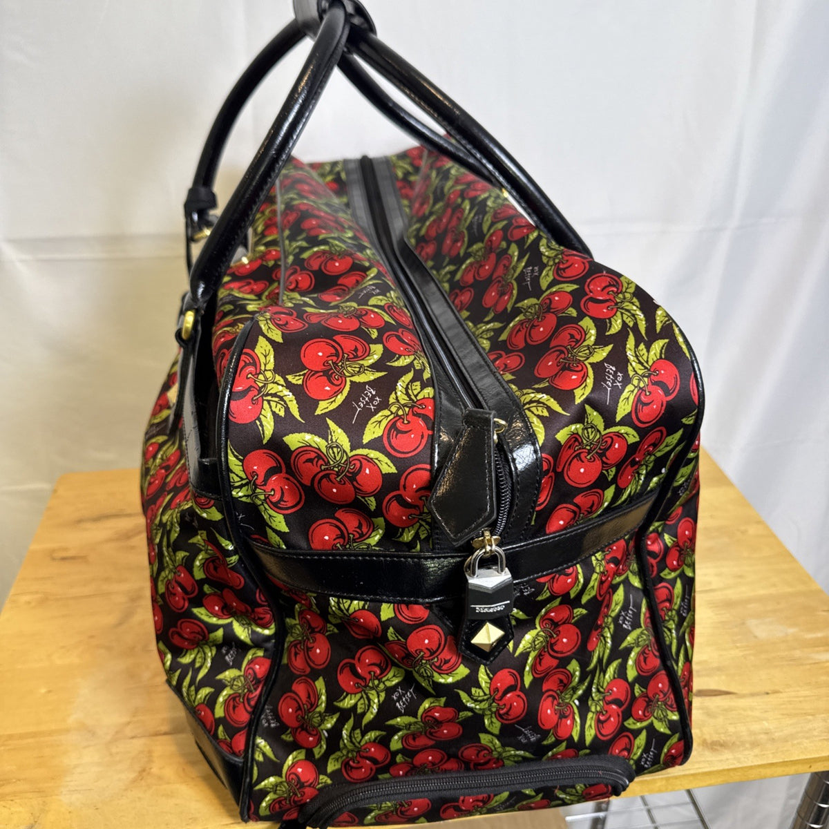 Betsey Johnson black rolling weekender duffel bag featuring a red cherry print and telescoping handle.