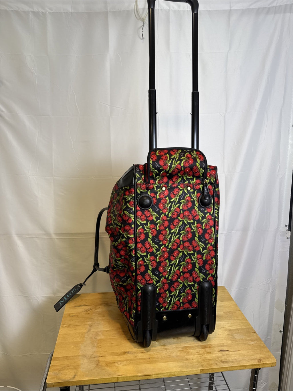 Betsey Johnson black rolling weekender duffel bag featuring a red cherry print and telescoping handle.