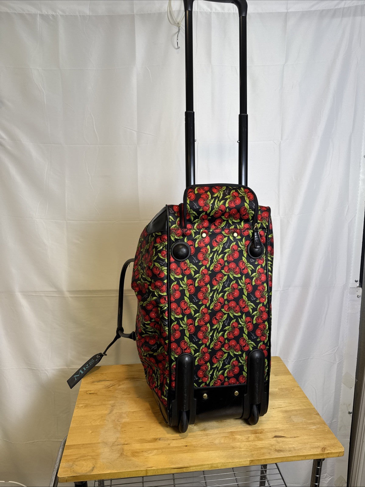 Betsey Johnson black rolling weekender duffel bag featuring a red cherry print and telescoping handle.