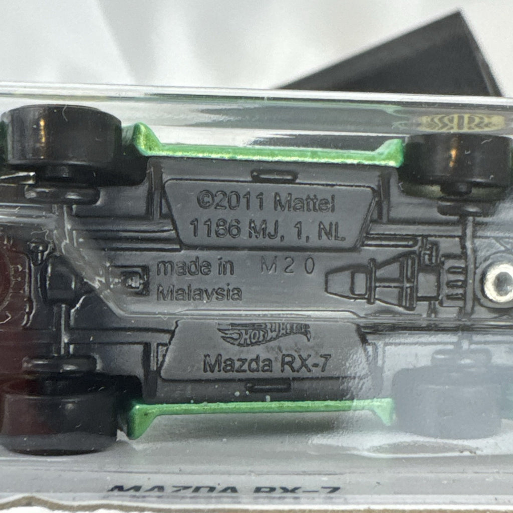 Hot Wheels 1:64 scale metallic green Mazda RX-7 diecast car with KONI graphics in factory sealed packaging.