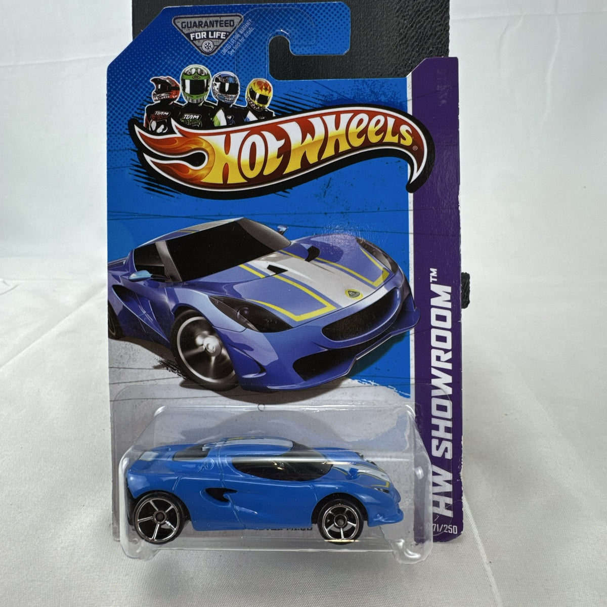 Blue Hot Wheels 1:64 scale Lotus M250 diecast car with white and yellow racing stripes sealed in original 2013 packaging.