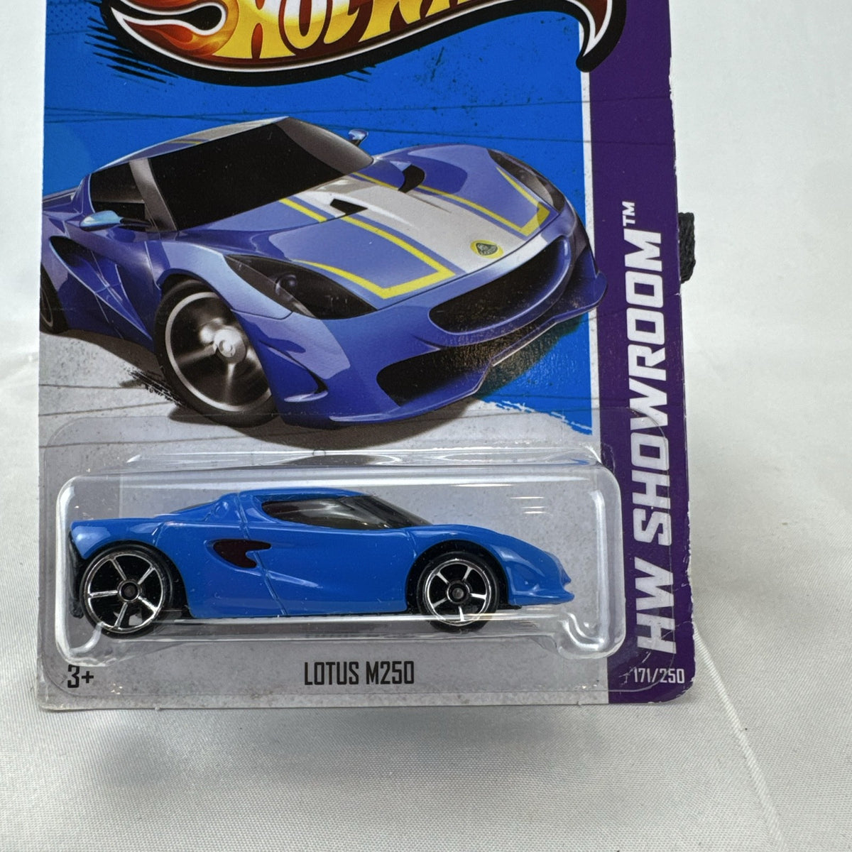 Blue Hot Wheels 1:64 scale Lotus M250 diecast car with white and yellow racing stripes sealed in original 2013 packaging.