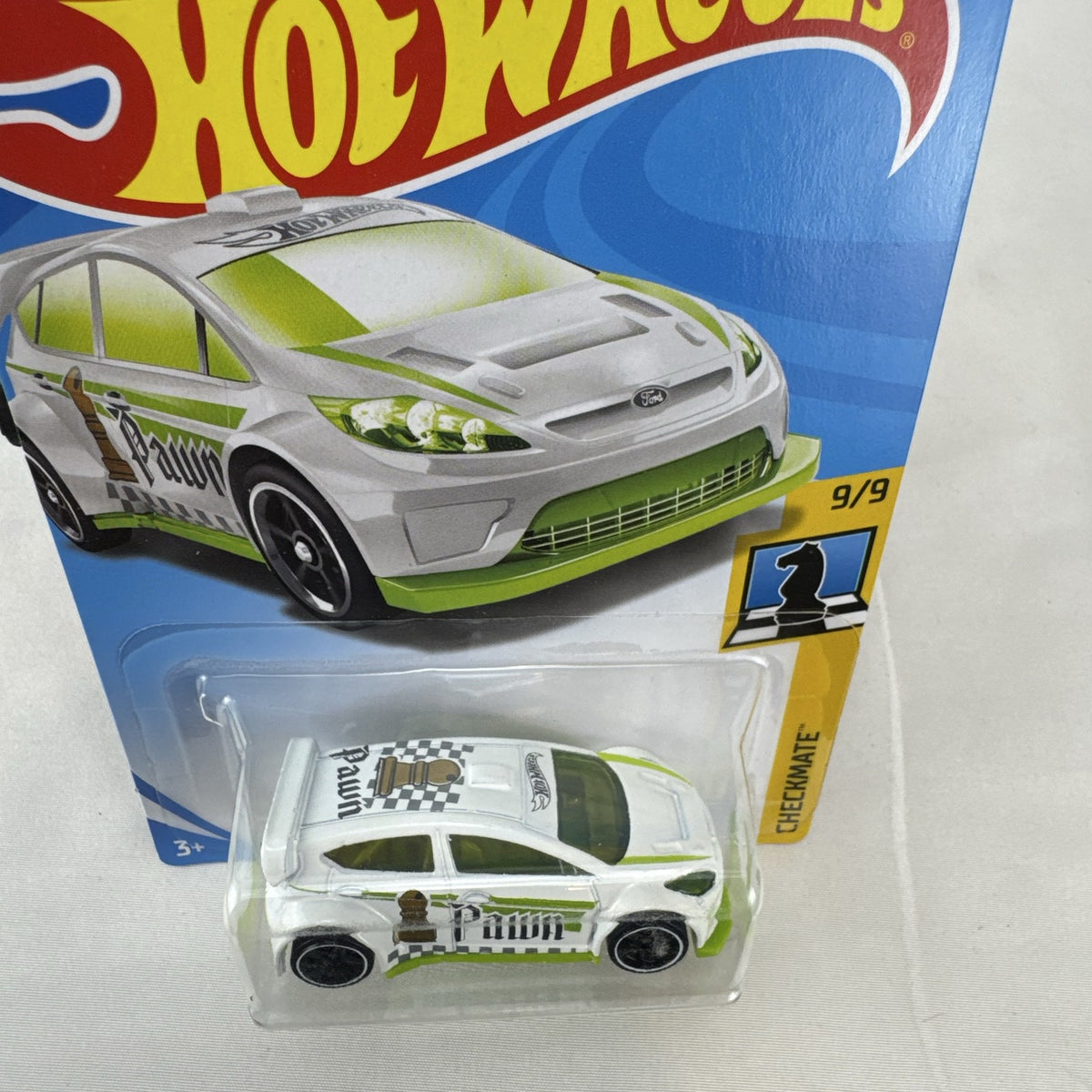 Hot Wheels 1:64 scale 2012 Ford Fiesta diecast car in white with green Pawn Checkmate graphics, sealed on card.