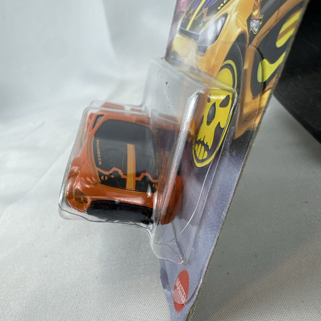Hot Wheels 1:64 scale Scorcher diecast car in orange with Halloween graphics and yellow skull rims in sealed packaging.
