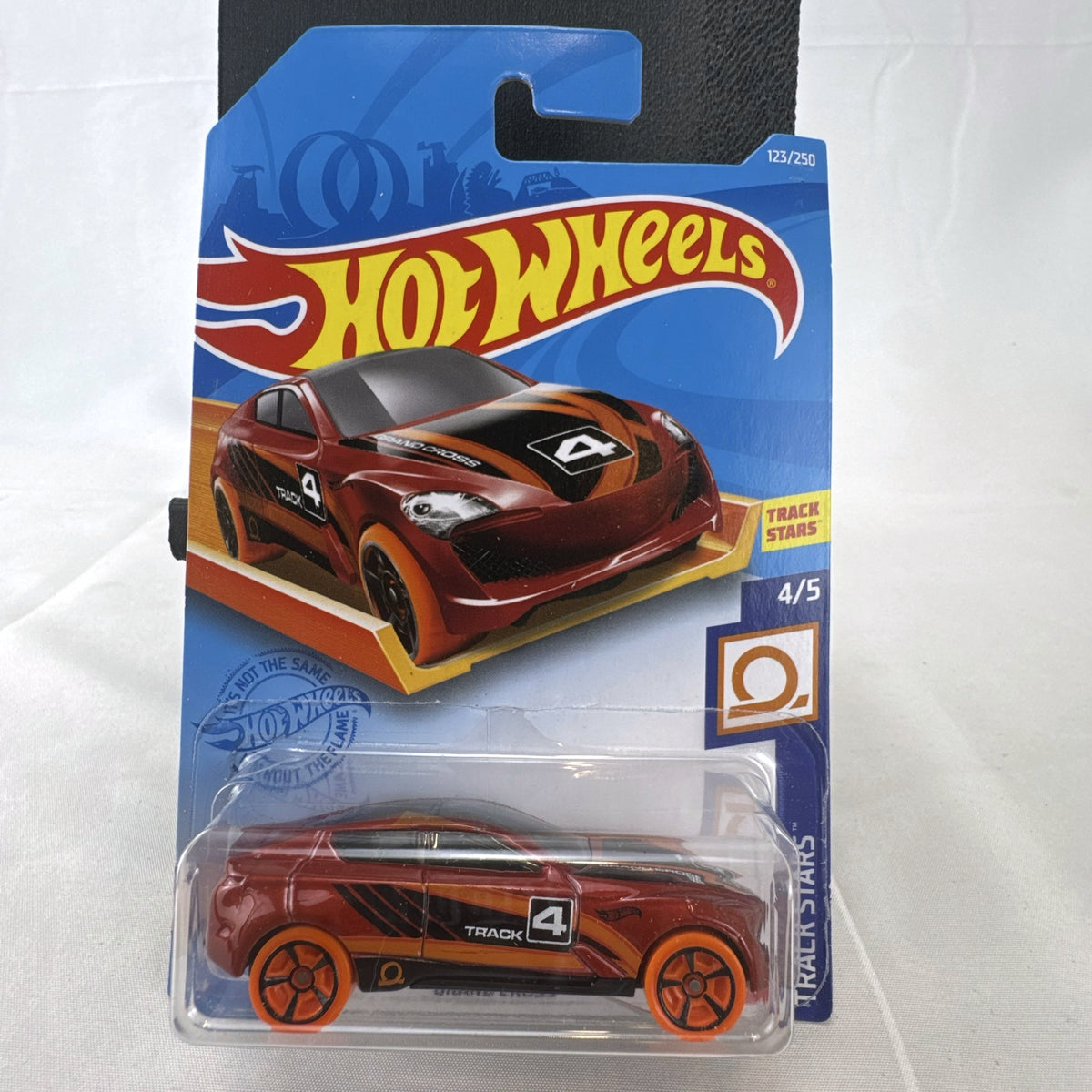 Sealed 1:64 scale Hot Wheels Grand Cross diecast car in metallic red with orange wheels and track stars graphics.