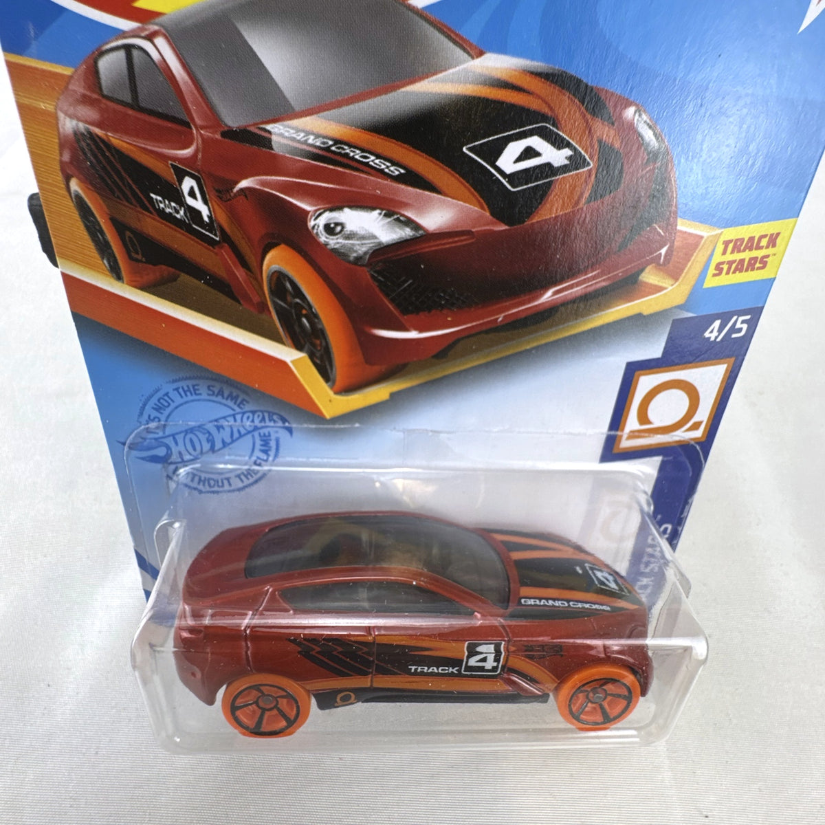 Hot Wheels Track Stars Grand Cross diecast racer in metallic red with orange wheels, sealed on card.