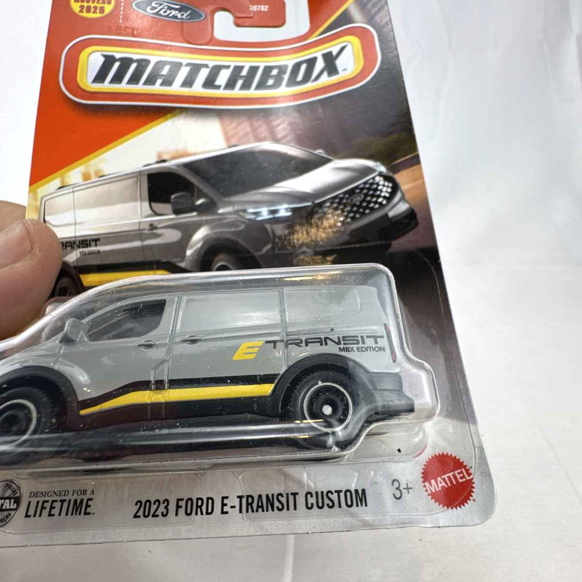Matchbox 2023 Ford E-Transit Custom diecast van in gray with MBX Edition livery, sealed on card.