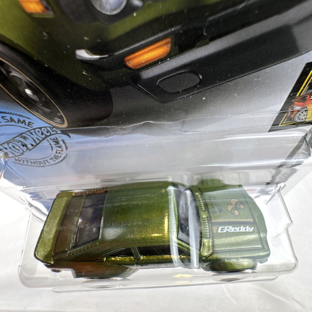 Hot Wheels 1:64 scale Mazda RX-3 diecast car in metallic olive green with GReddy graphics on blister card