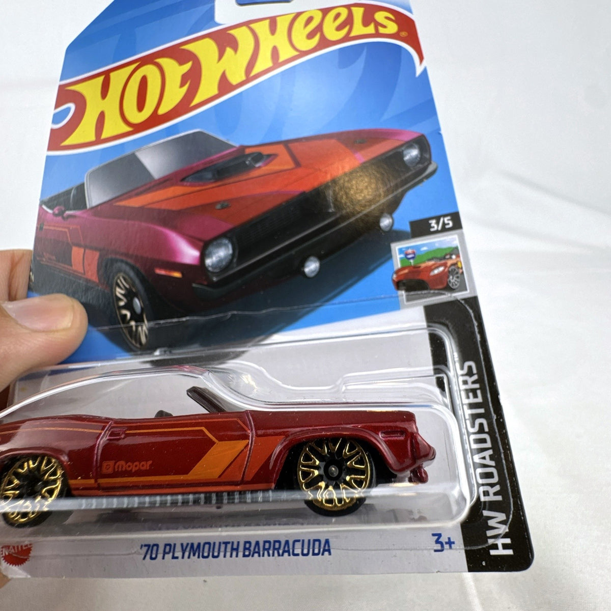 Hot Wheels 1:64 scale 1970 Plymouth Barracuda convertible diecast car in metallic red with gold wheels in sealed package.