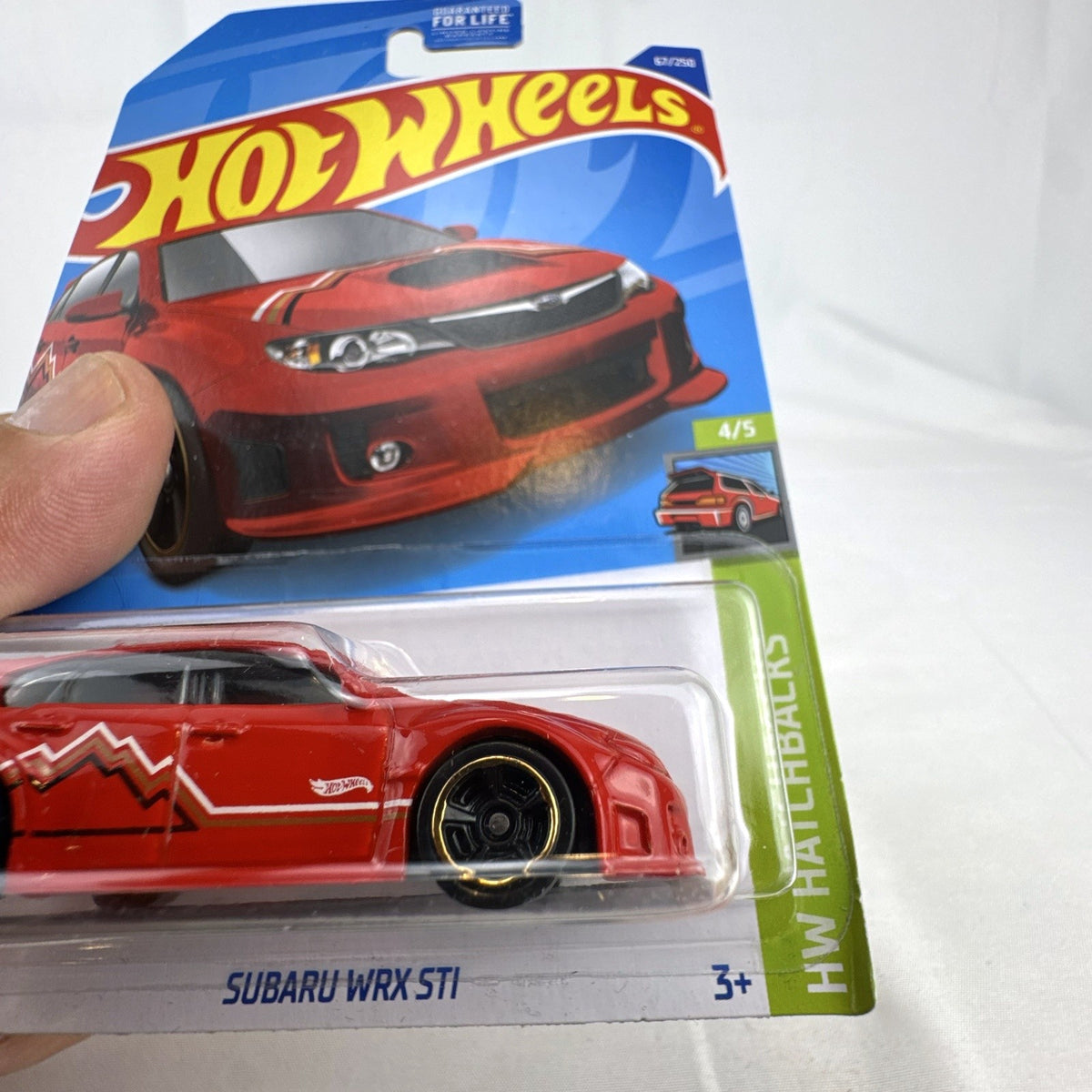 Hot Wheels 1:64 scale Subaru WRX STI diecast car in red sealed on HW Hatchbacks card packaging.