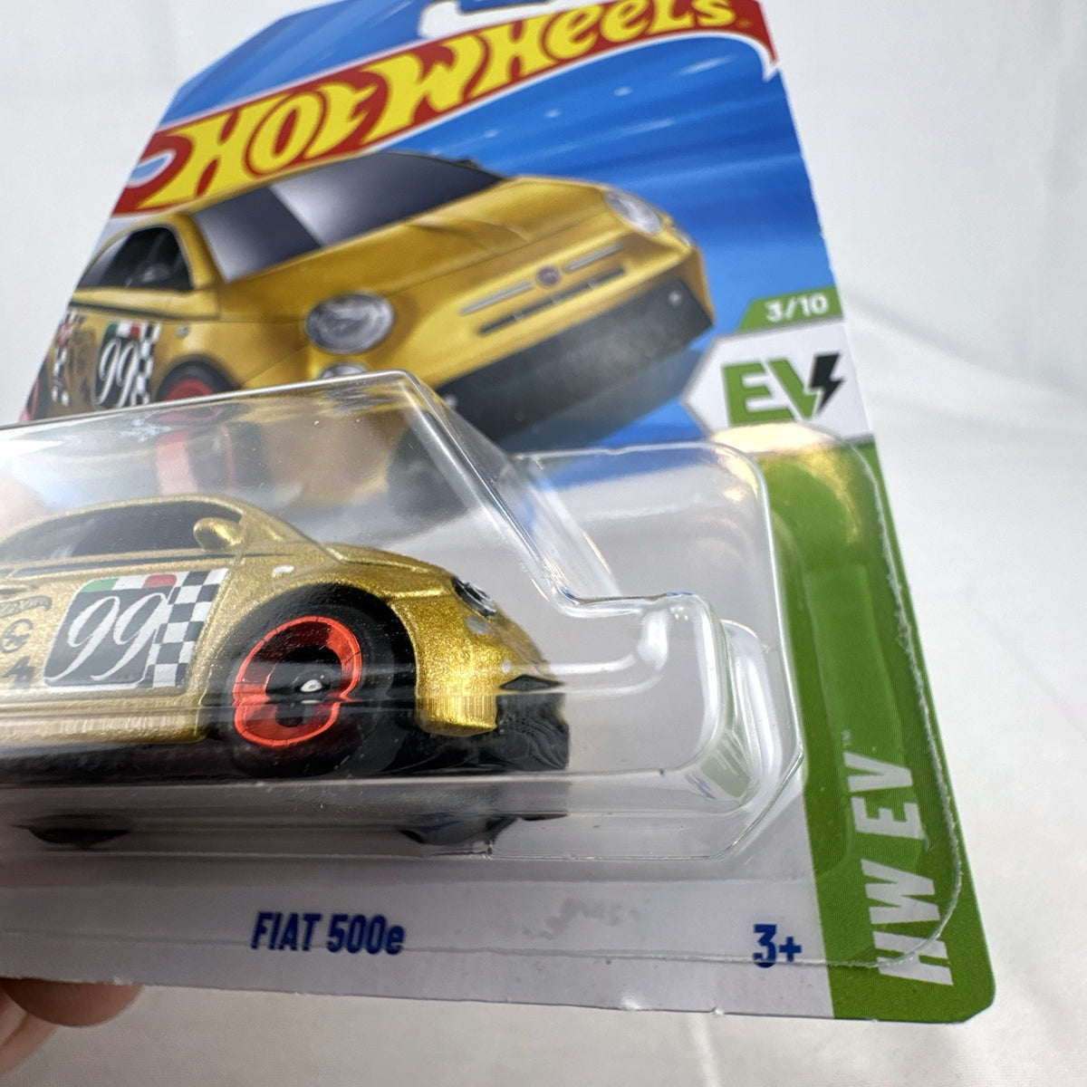 Hot Wheels 1:64 scale FIAT 500e diecast car in metallic gold with #99 racing graphics in sealed card packaging.