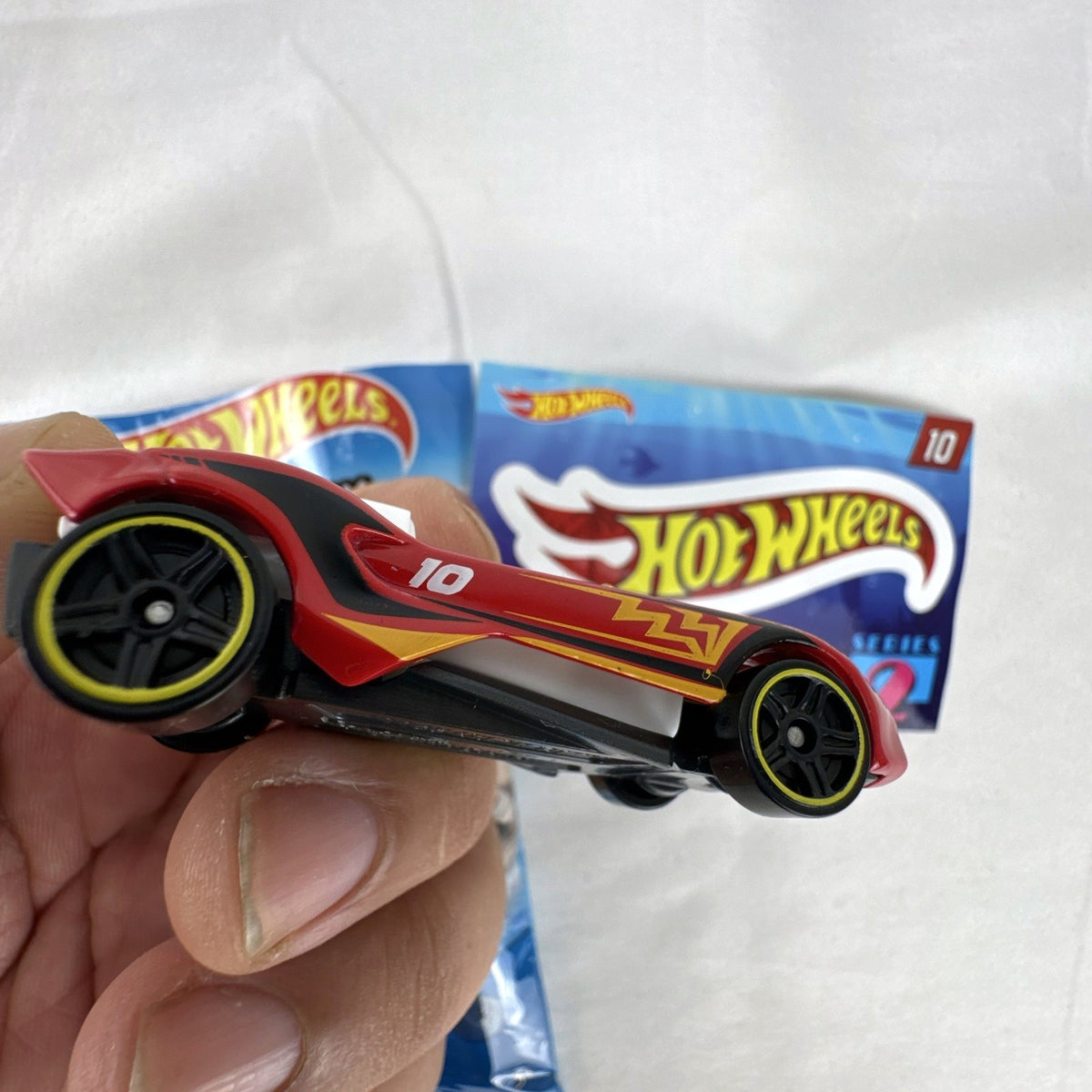 Red Hot Wheels Carbonic 1:64 scale diecast car from Mystery Models Series 2 with yellow graphics and opened foil pouch.