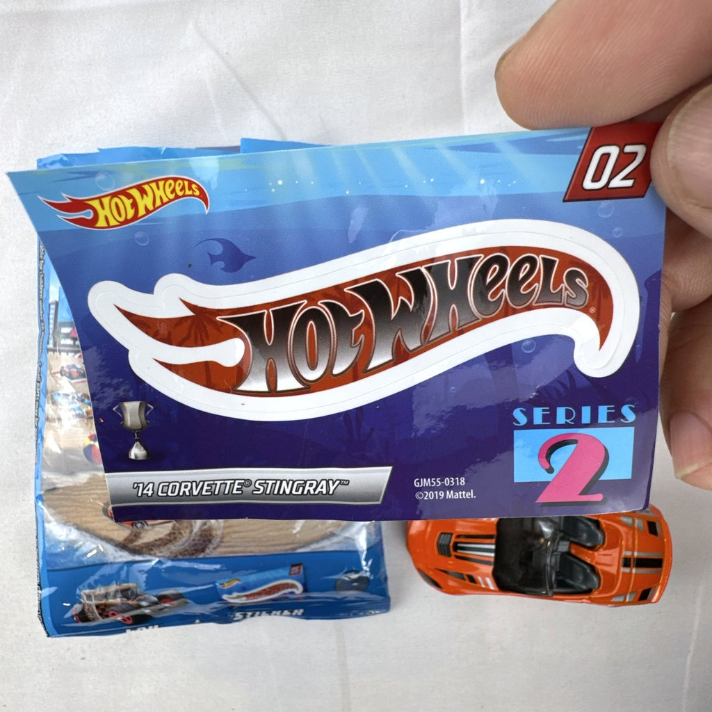 Orange Hot Wheels 1:64 scale 2014 Chevrolet Corvette Stingray diecast car with racing stripes and mystery model packaging.