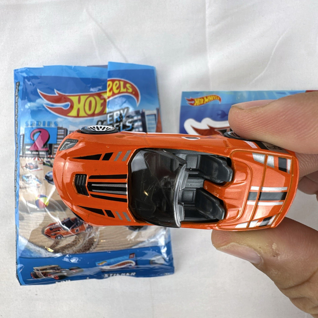 Orange Hot Wheels 1:64 scale 2014 Chevrolet Corvette Stingray diecast car with racing stripes and mystery model packaging.