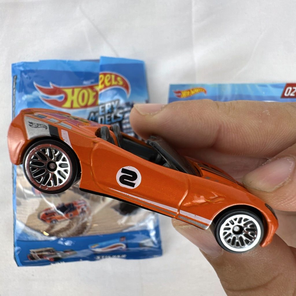 Orange Hot Wheels 1:64 scale 2014 Chevrolet Corvette Stingray diecast car with racing stripes and mystery model packaging.