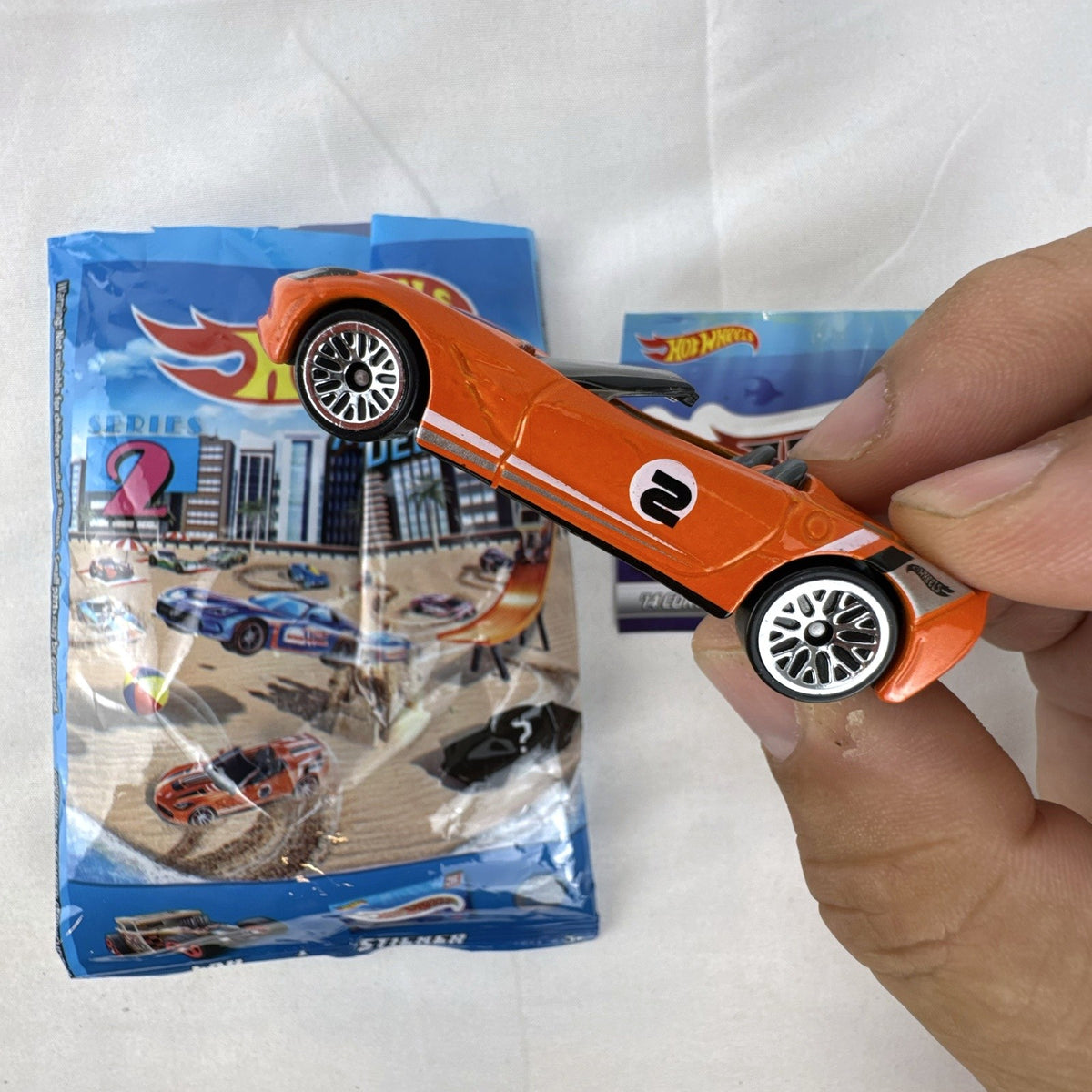 Orange Hot Wheels 1:64 scale 2014 Chevrolet Corvette Stingray diecast car with racing stripes and mystery model packaging.