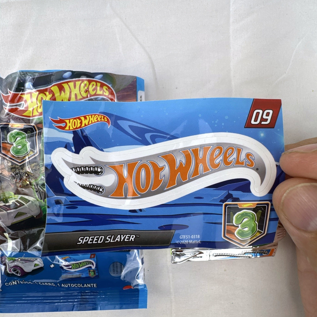 Hot Wheels Speed Slayer 1:64 scale diecast car in chrome with orange base, lime green canopy, foil bag, and sticker.