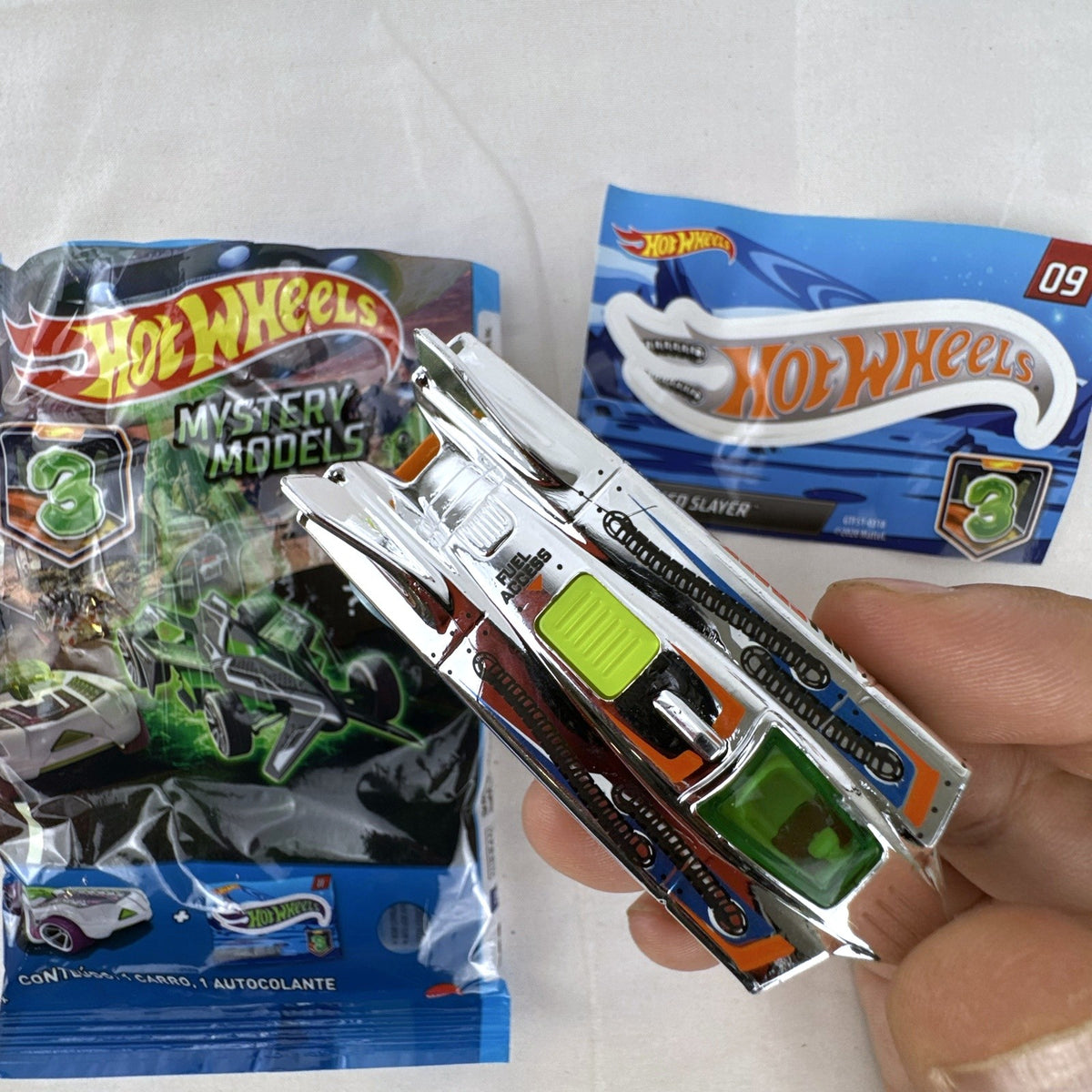 Hot Wheels Speed Slayer 1:64 scale diecast car in chrome with orange base, lime green canopy, foil bag, and sticker.