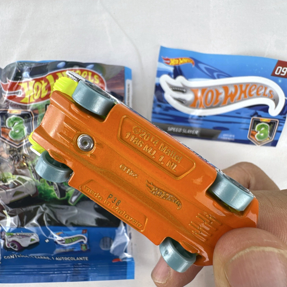Hot Wheels Speed Slayer 1:64 scale diecast car in chrome with orange base, lime green canopy, foil bag, and sticker.