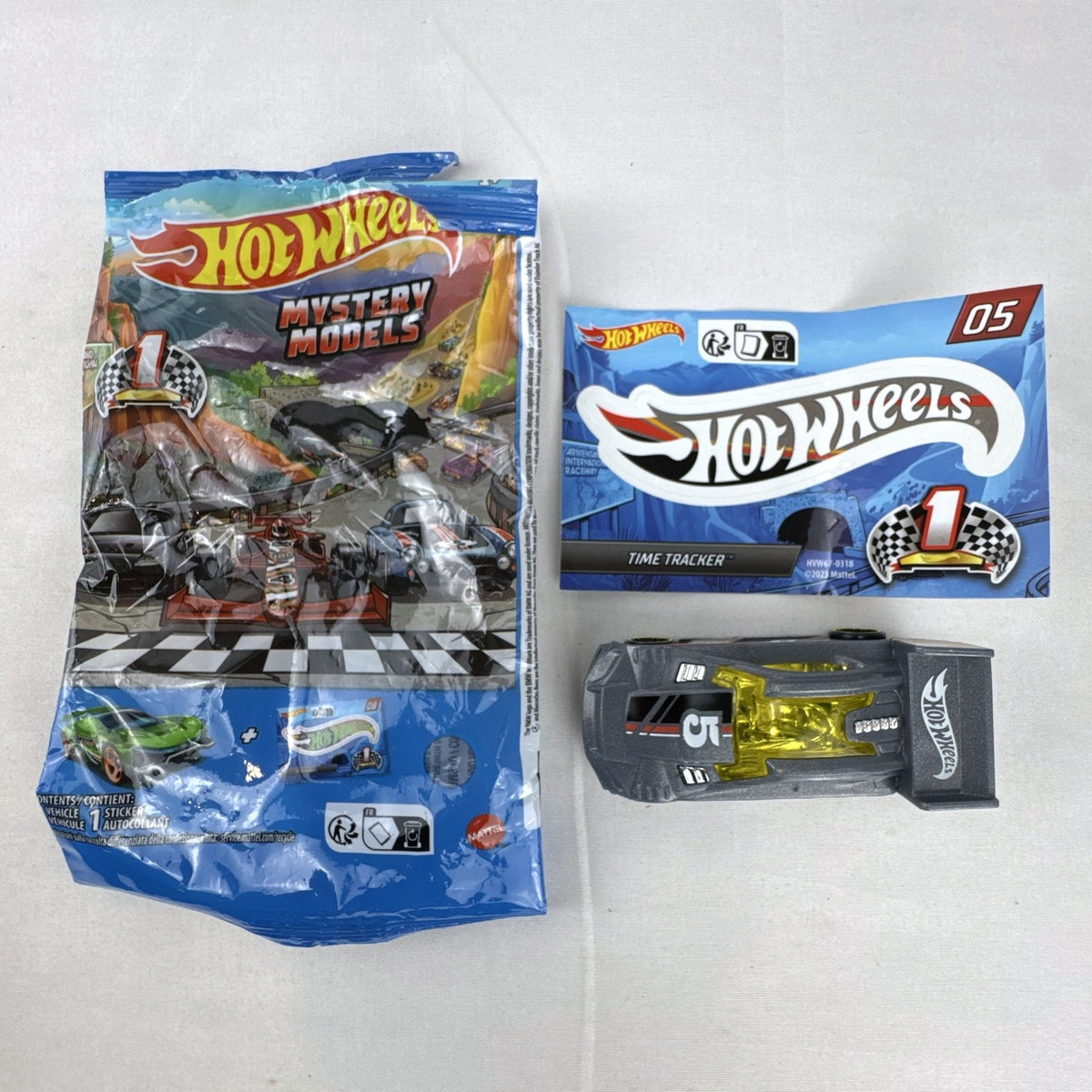 Dark gray Hot Wheels Time Tracker diecast car 1:64 scale with yellow wheels and mystery models sticker sheet.