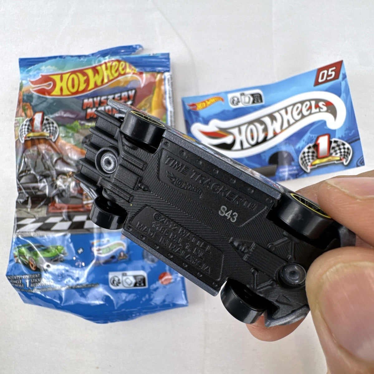 Dark gray Hot Wheels Time Tracker diecast car 1:64 scale with yellow wheels and mystery models sticker sheet.