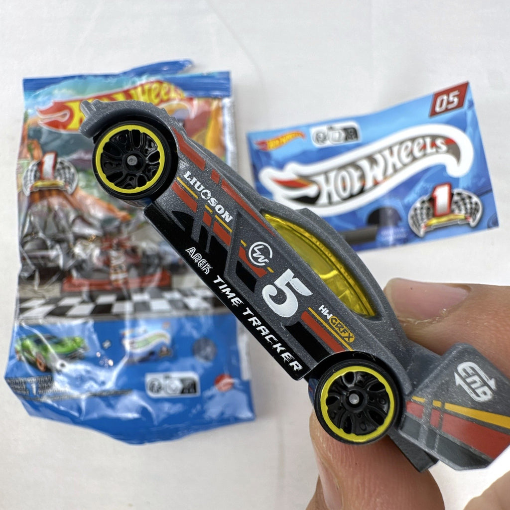 Dark gray Hot Wheels Time Tracker diecast car 1:64 scale with yellow wheels and mystery models sticker sheet.