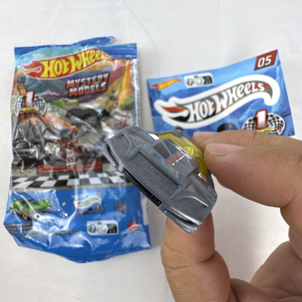 Dark gray Hot Wheels Time Tracker diecast car 1:64 scale with yellow wheels and mystery models sticker sheet.