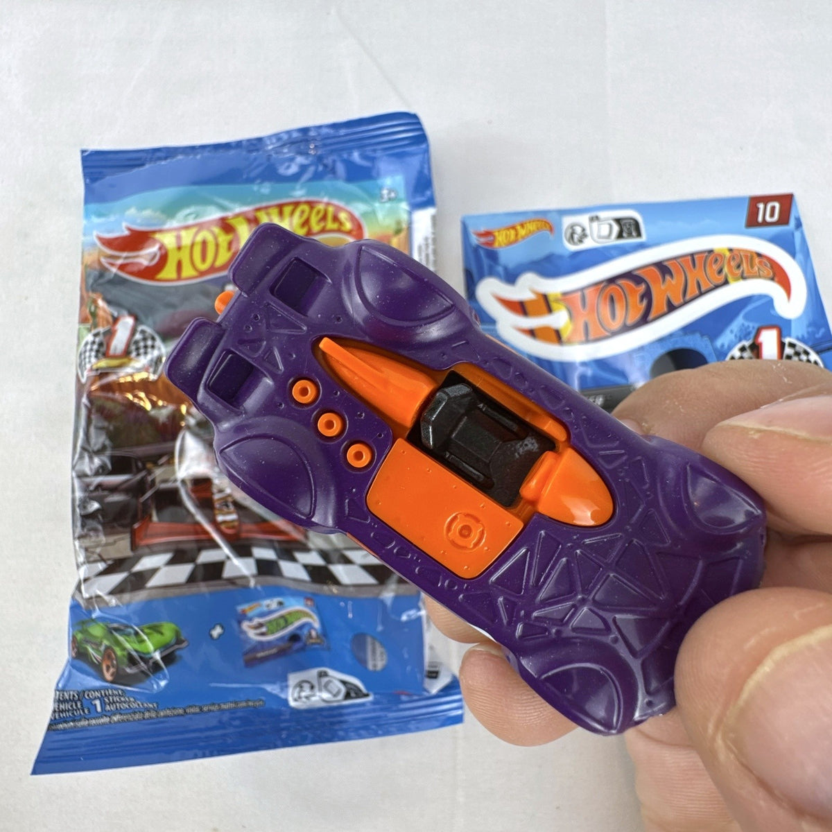 Hot Wheels 1:64 scale Monteracer diecast car in purple and orange from Mystery Models Series 1 with original bag and sticker.