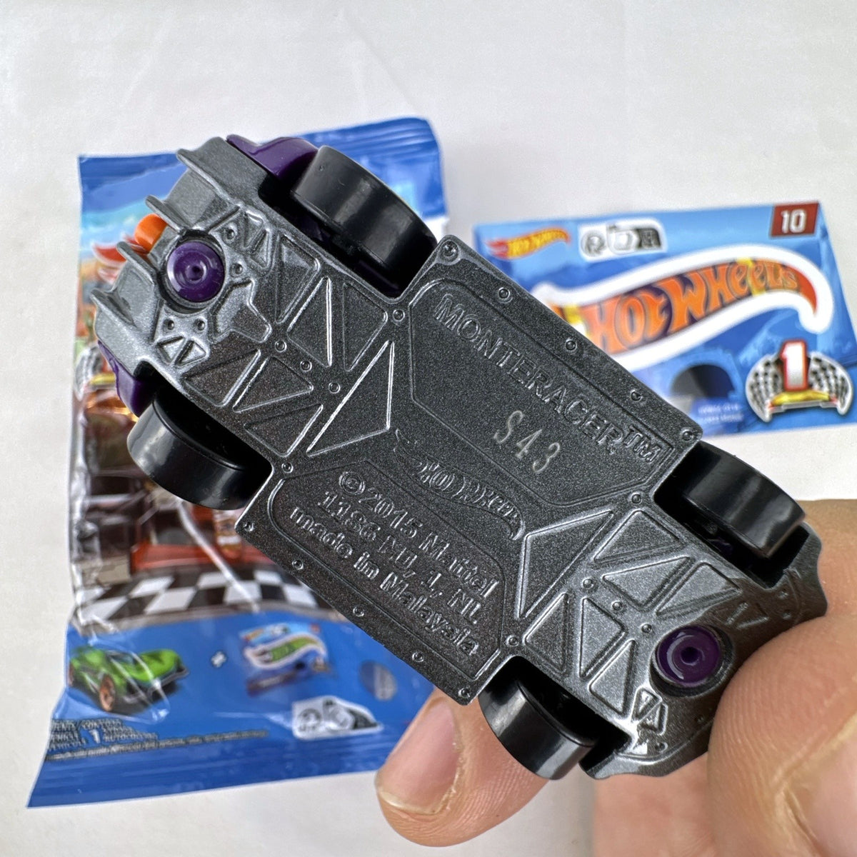 Hot Wheels 1:64 scale Monteracer diecast car in purple and orange from Mystery Models Series 1 with original bag and sticker.
