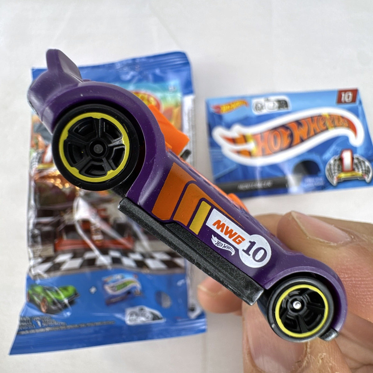 Hot Wheels 1:64 scale Monteracer diecast car in purple and orange from Mystery Models Series 1 with original bag and sticker.