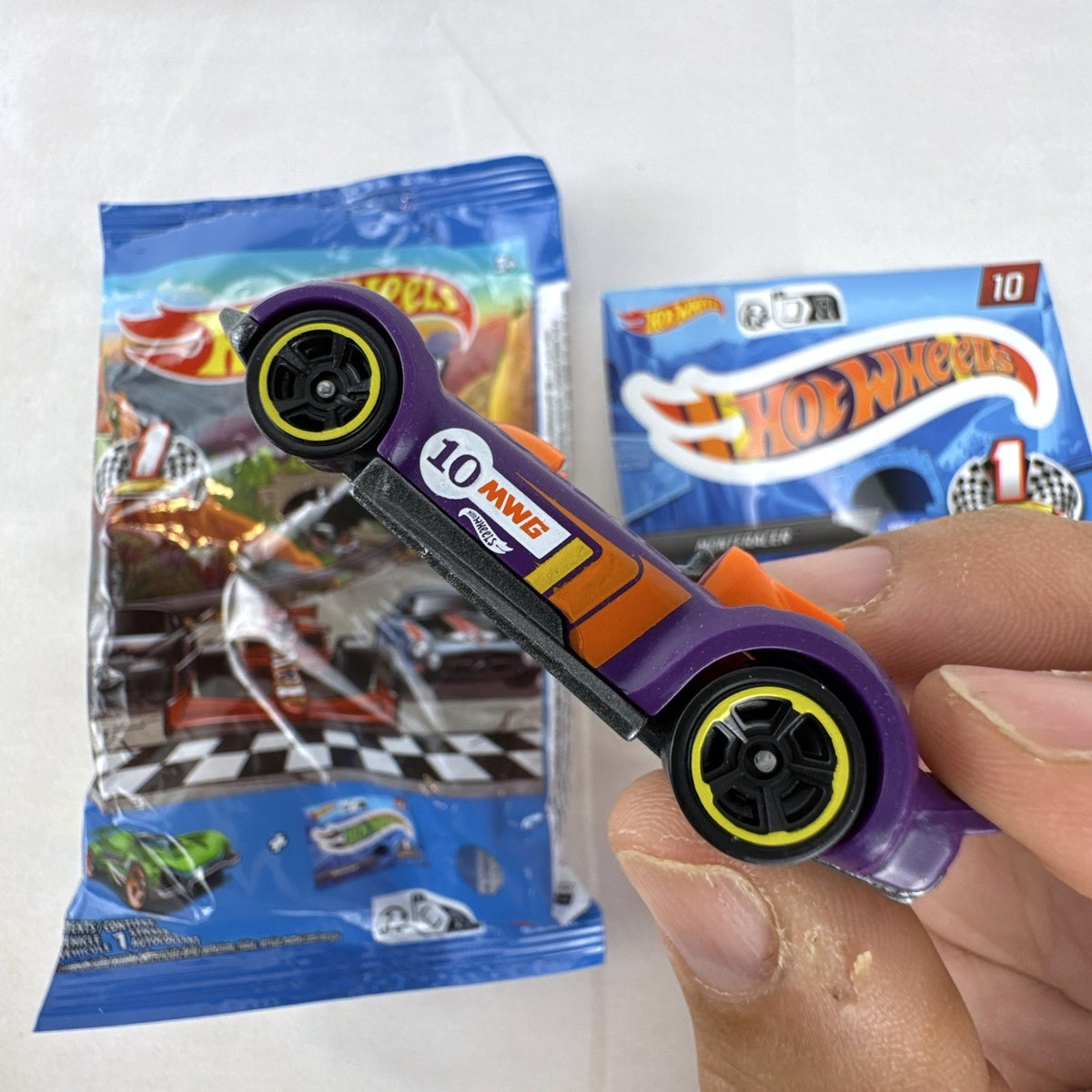 Hot Wheels 1:64 scale Monteracer diecast car in purple and orange from Mystery Models Series 1 with original bag and sticker.