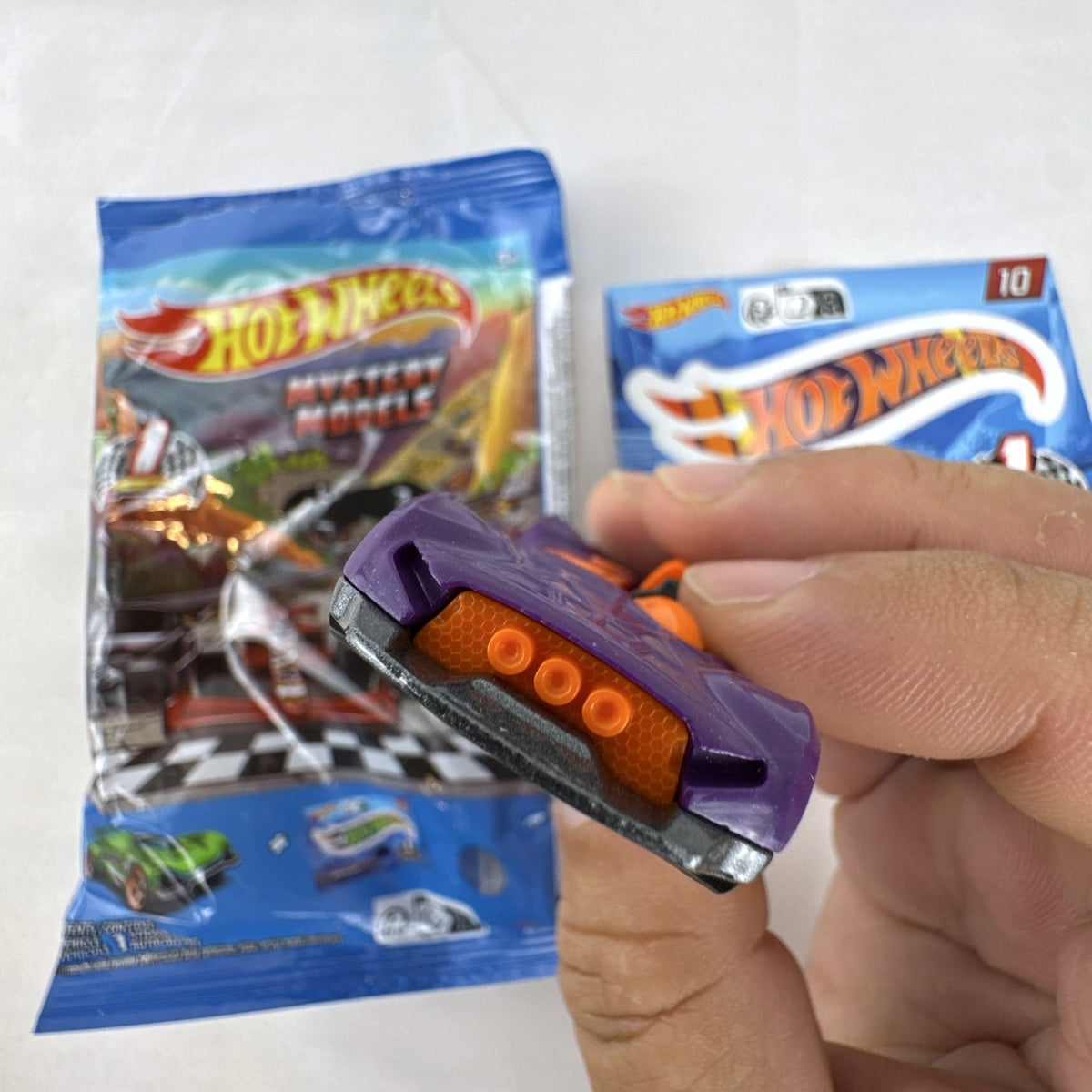 Hot Wheels 1:64 scale Monteracer diecast car in purple and orange from Mystery Models Series 1 with original bag and sticker.