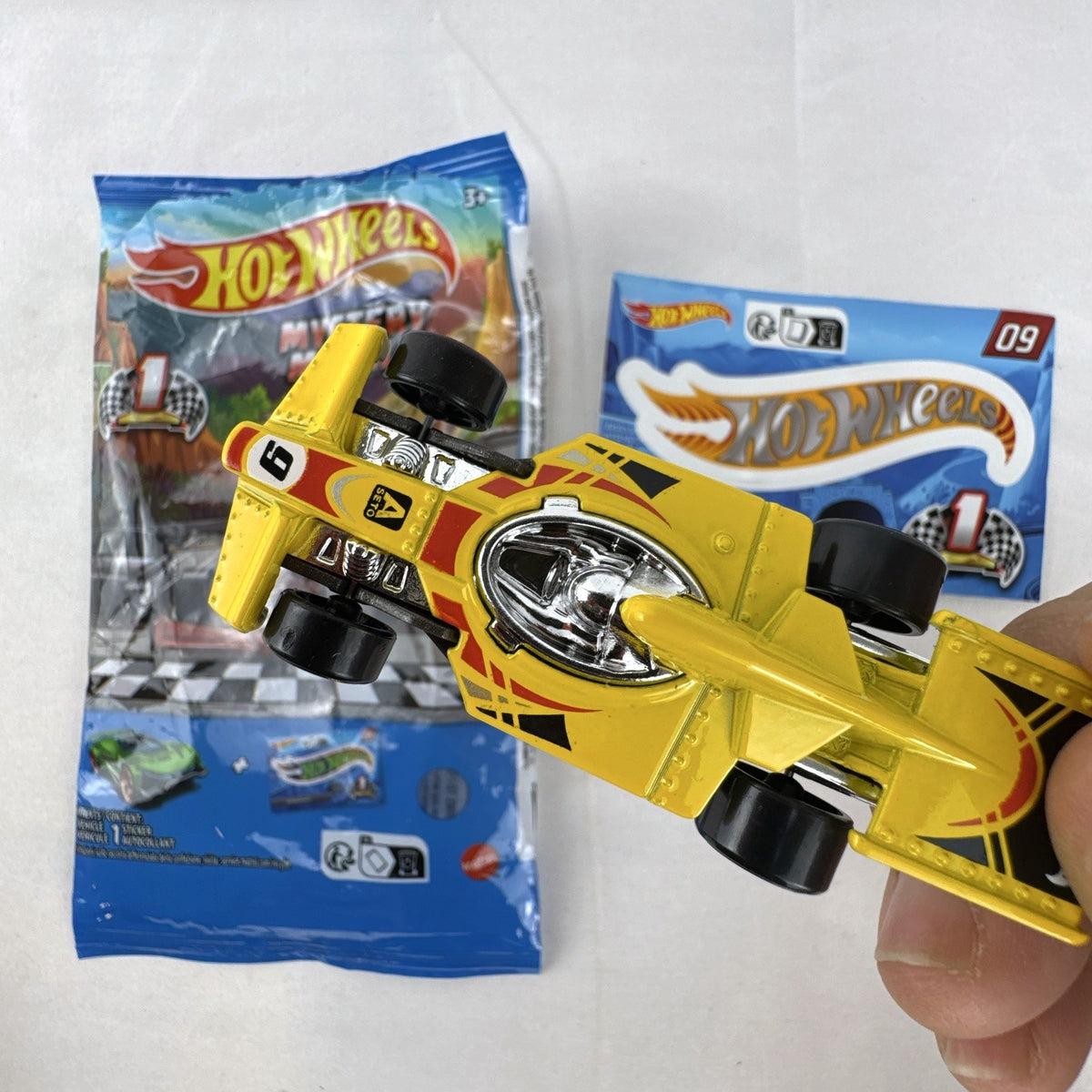 Hot Wheels 1:64 scale Formula Flashback Mystery Models Series 1 yellow diecast racer with sticker card and opened foil pouch