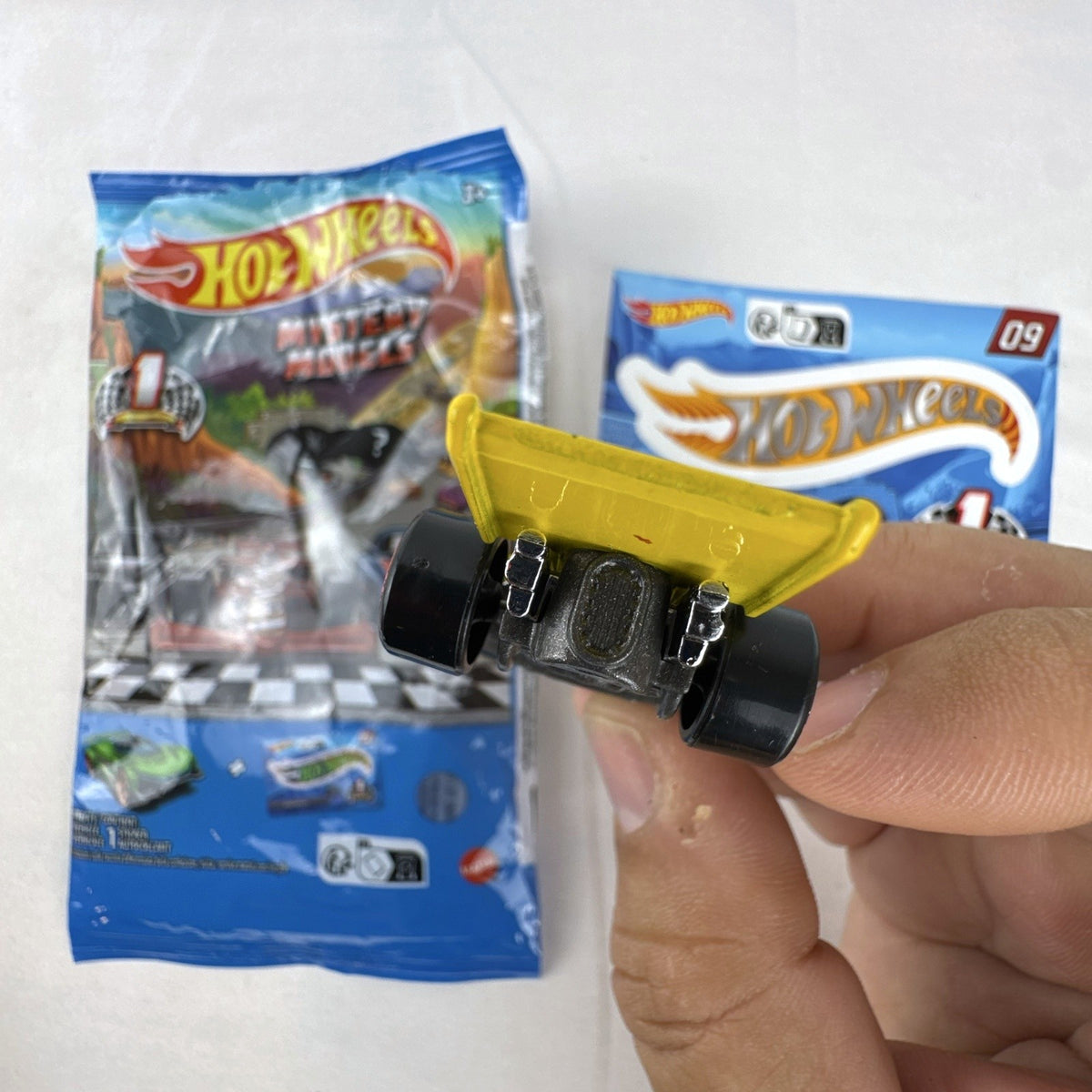 Hot Wheels 1:64 scale Formula Flashback Mystery Models Series 1 yellow diecast racer with sticker card and opened foil pouch