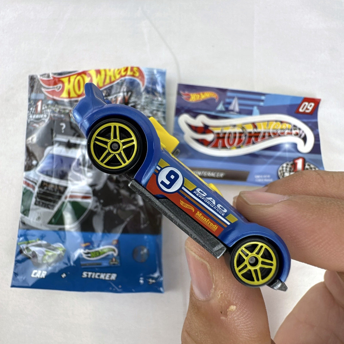 Blue 1:64 scale Hot Wheels Monteracer #09 Mystery Models diecast car with red and yellow graphics.