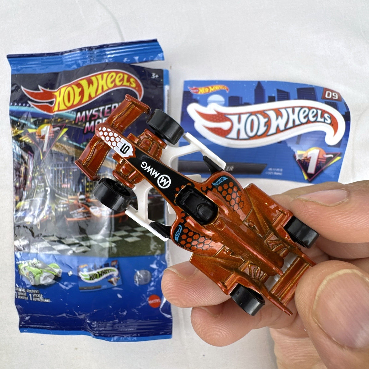 Hot Wheels 1:64 scale F1 Racer diecast car in metallic copper orange with original Mystery Models foil pouch and sticker